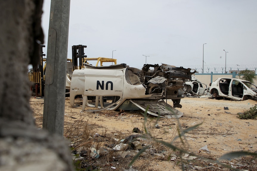 Image of a white vehicle with black letters UN on it, it's badly damaged and lies upside down.