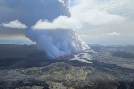 A large plume of smoke billows from a bright orange crack in the ground against a vast landscape