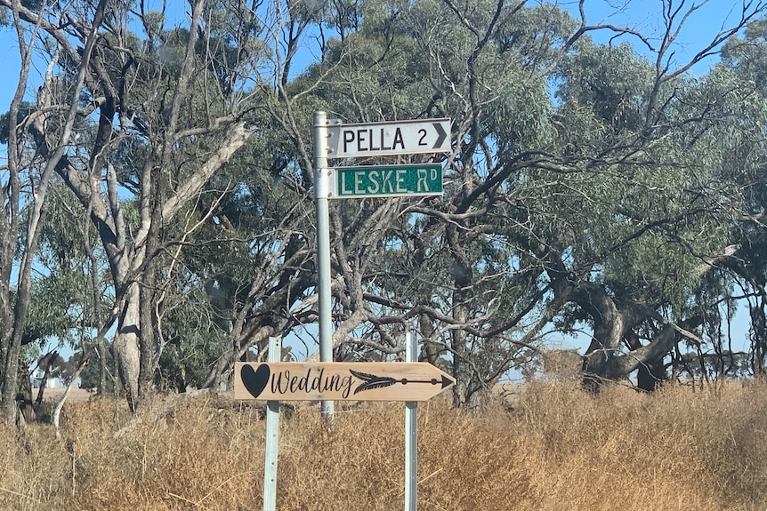 A white sign reading 'Pella 2' points to the right above a wooden sign reading 'wedding' against a bush backdrop