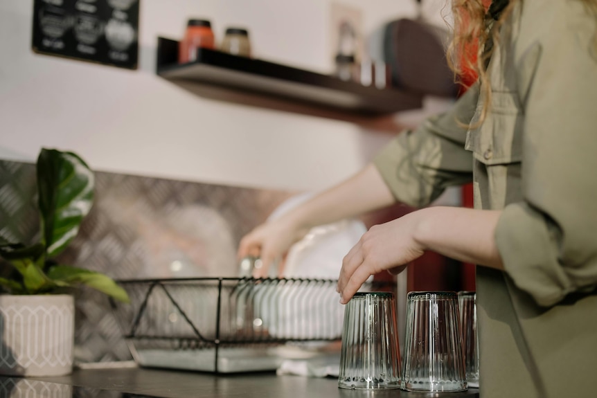 woman in a gray shirt is washing and drying glasses and dishes in the kitchen 