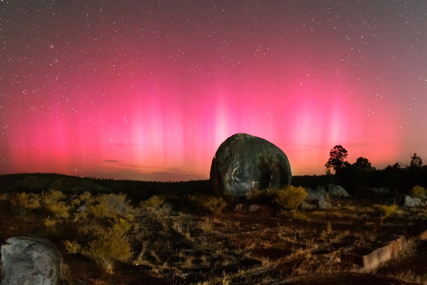 A glowing pink sky with a boulder in the foreground.