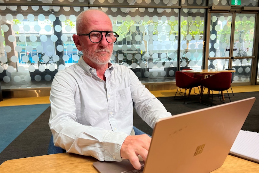 a bald white man wearing glasses typing at a laptop