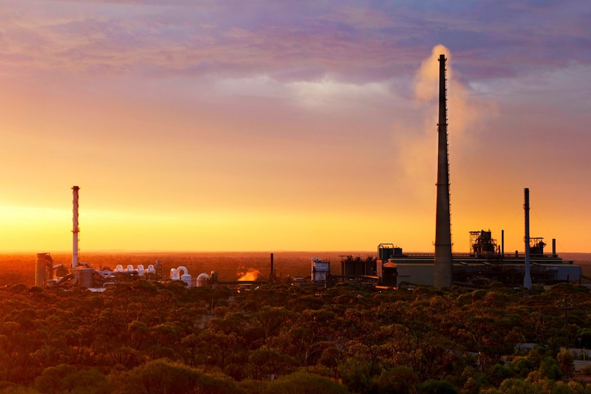 Sunset at a mining operation with a big smoke stack.  