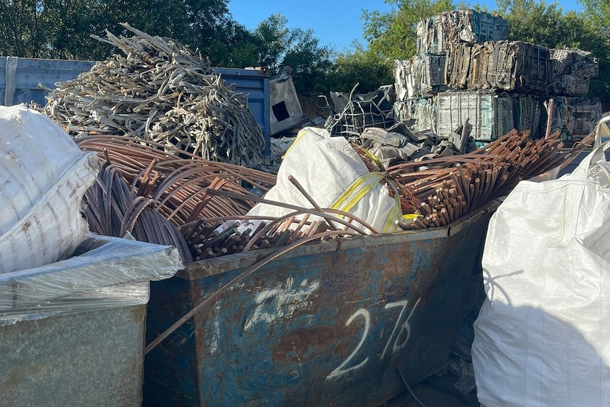 A large pile of copper sits in a skip bin in a car park.