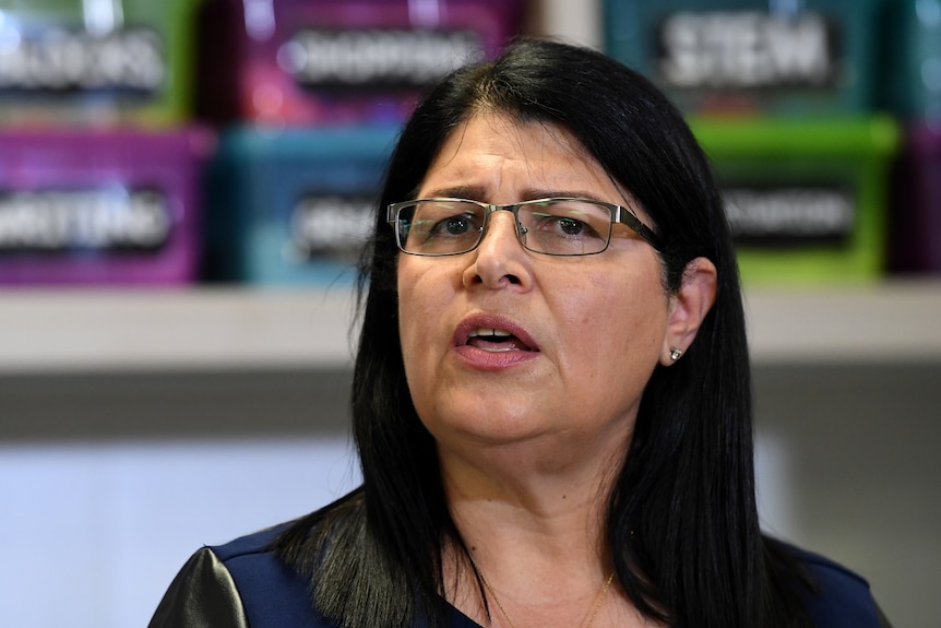 A dark-haired, bespectacled woman in mid-sentence.