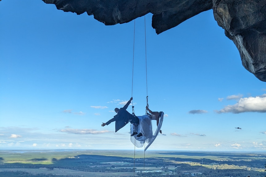 Newlyweds abseiling in front of a cave.