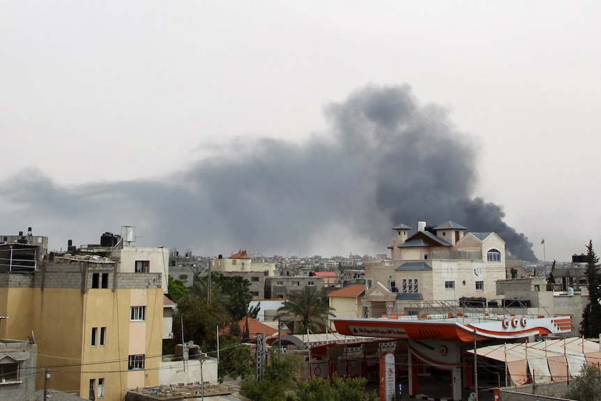 Image of houses, behind them a large plume of smoke rises.