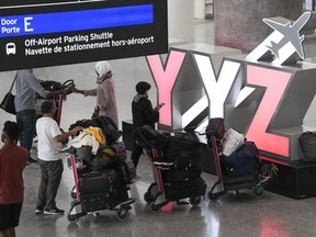 People wait with their luggage at Pearson International Airport in Toronto on Friday, August 5, 2022. A ruling from the Canadian Transportation Agency says that a couple who called to cancel their booking on a flight that had already been cancelled by the airline means they are not entitled to a refund.