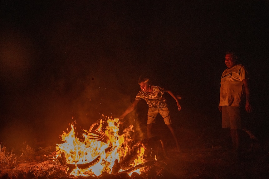 A boy throws a kangaroo into a camp fire 