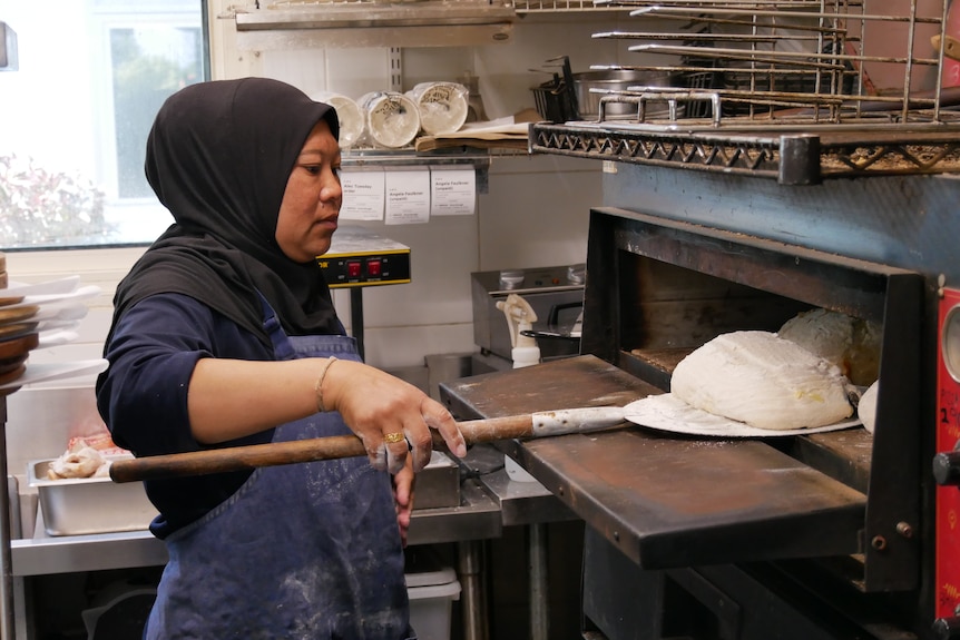 A woman places loaves into an oven for baking.