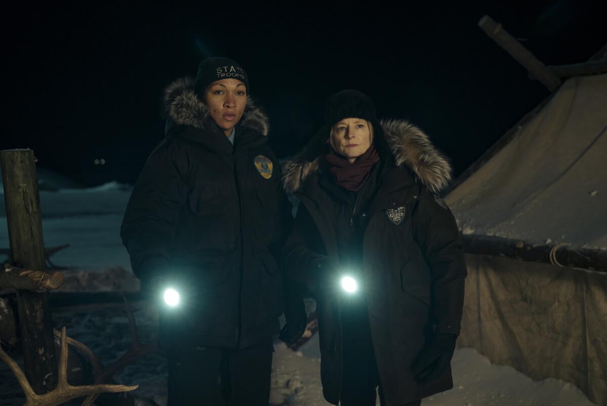 Two law enforcement officers in heavy parkas shine flashlights into an encampment