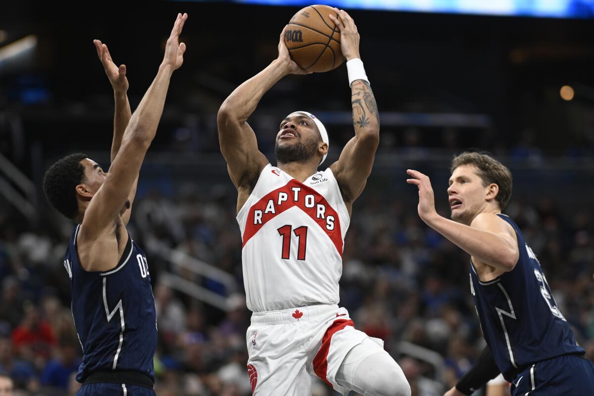 Raptors forward Bruce Brown, center shoots between Orlando's Caleb Houstan, left, Moritz Wagner.