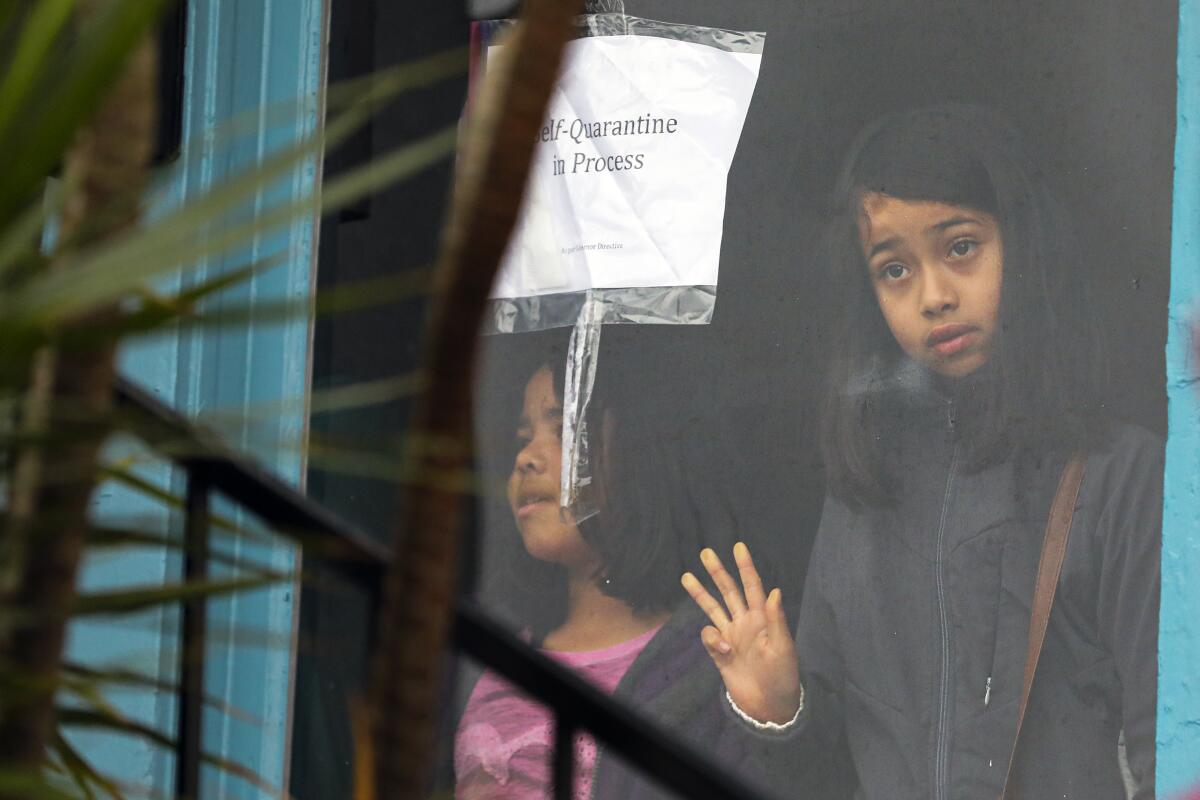 Two sisters stand in the window of a vacant house that they and their mother occupied in March 2020.