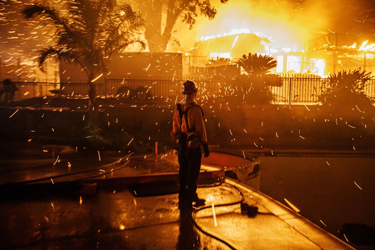 Embers from a burning home blow toward a firefighter.