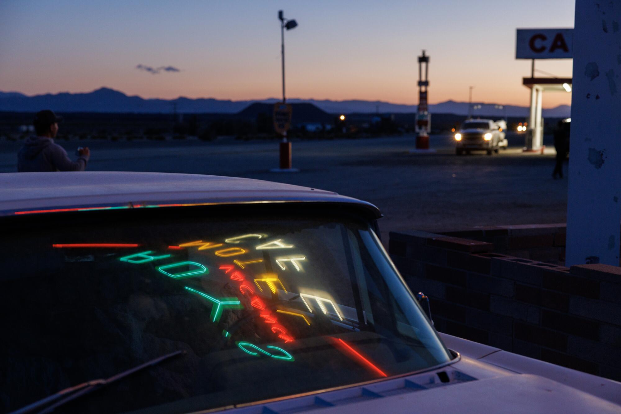 Roy's Motel and Cafe sign is reflected in the windshield of a vintage vehicle parked next to the sign.