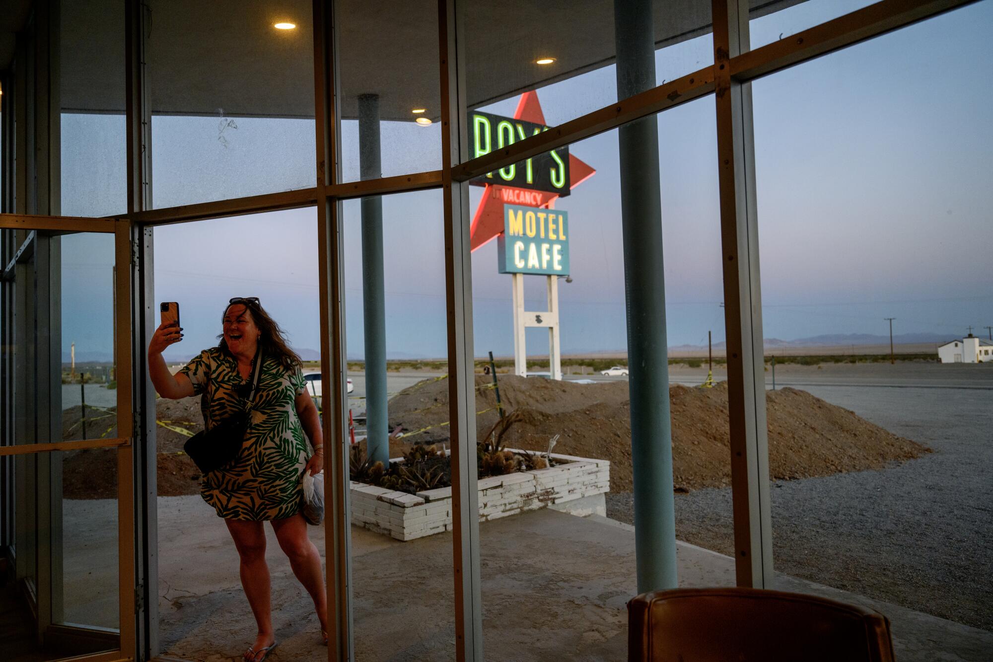 A woman takes a selfie with the Roy's Motel and Cafe sign behind her.