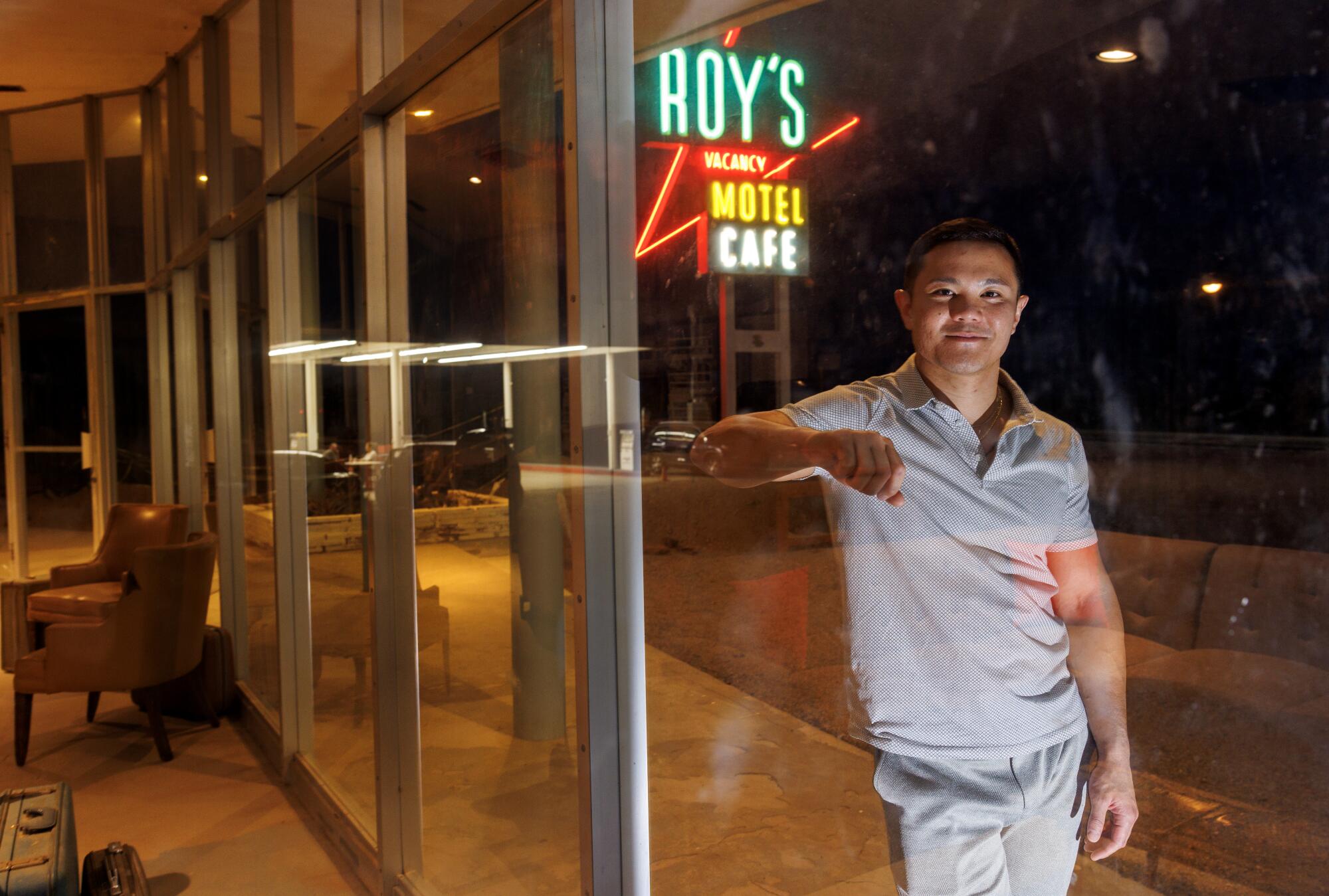 Kyle Okura leans on a glass window, with the Roy's neon sign behind him.