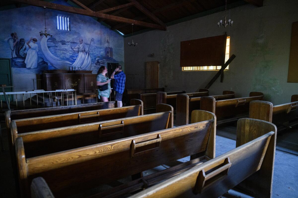 Two people stand near the front of a church, with empty pews.