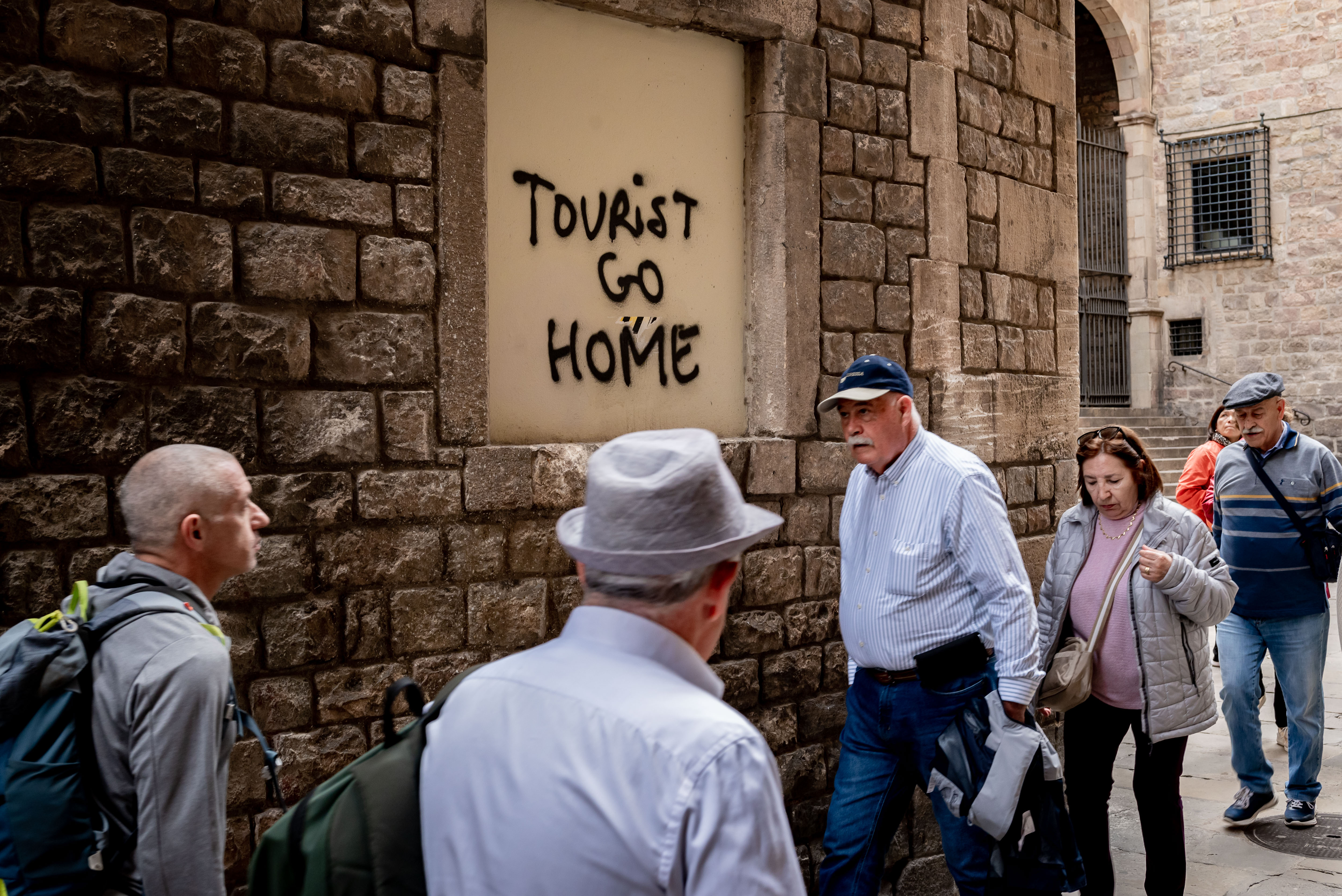 People walk past graffiti against tourism reading 'Tourist go home'