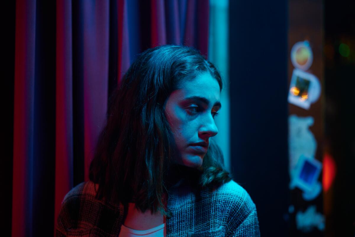 A woman stands backstage looking to one side, lighted by a blue light