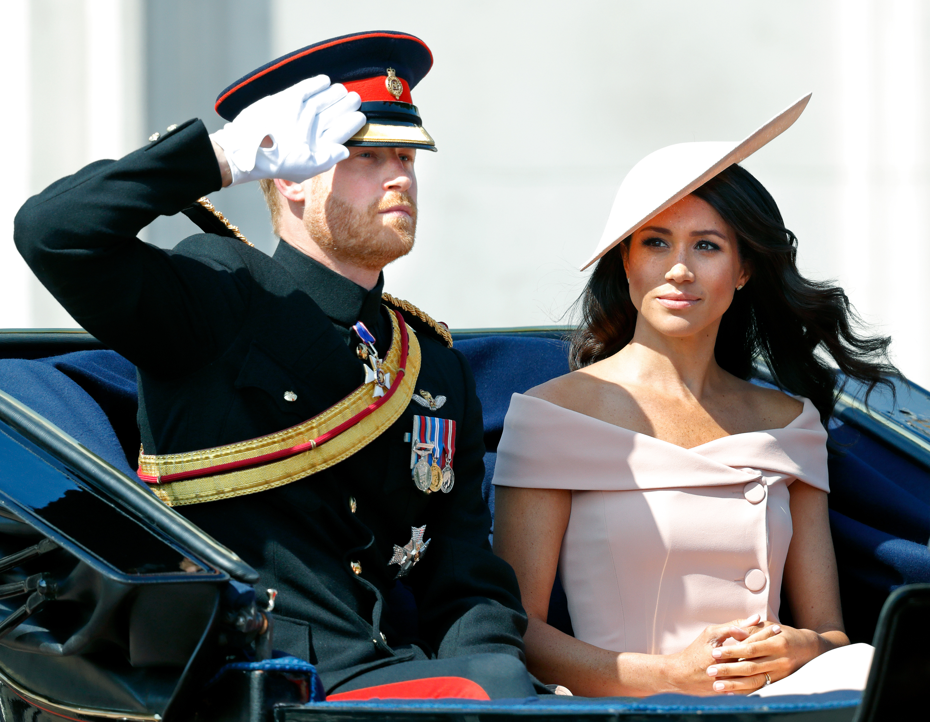 The Duke in 2018 donning military garments and saluting crowds as wife Meg sits next to him