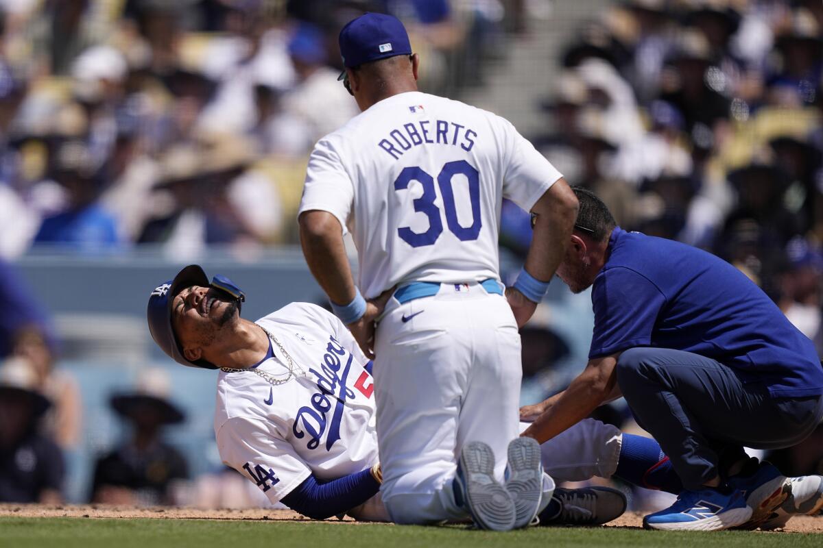 Mookie Betts, left, writhes on the ground after being hit by a pitch as manager Dave Roberts and a team trainer tend to him.