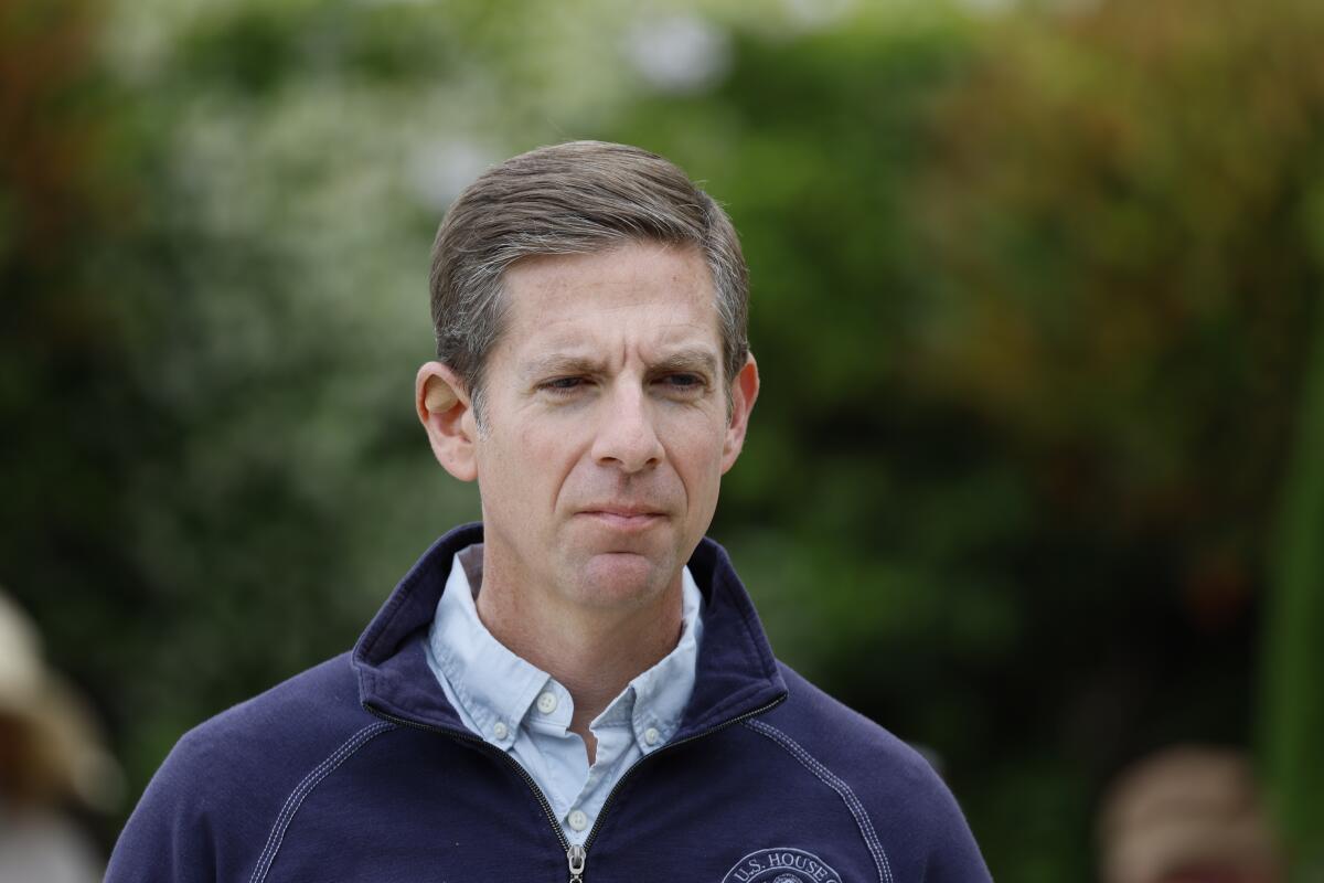 Rep. Mike Levin pictured from the shoulders up in front of green foliage, in a zippered blue sweater over a collared shirt