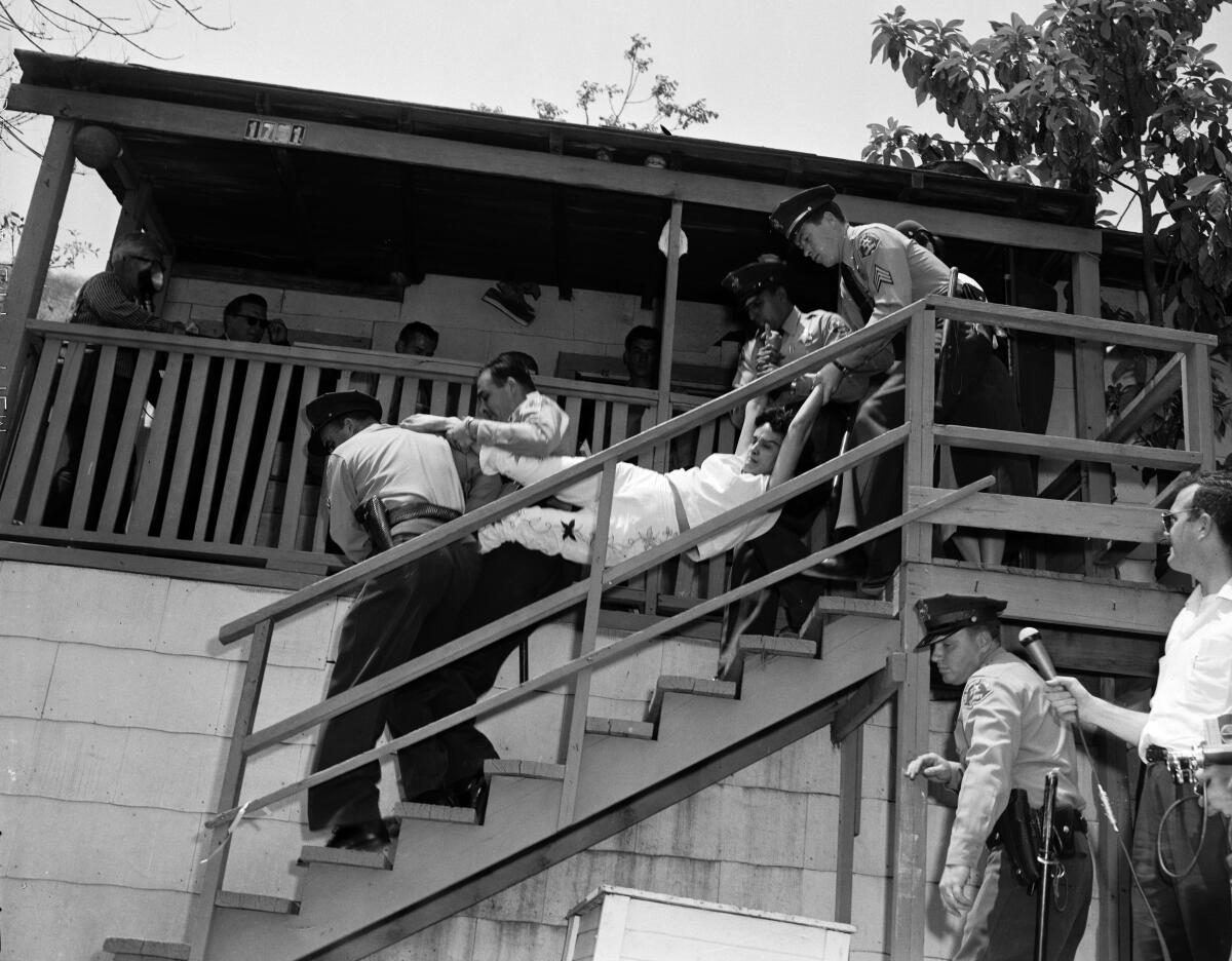 A black and white photo of a woman being carried down a staircase by law enforcement officers.