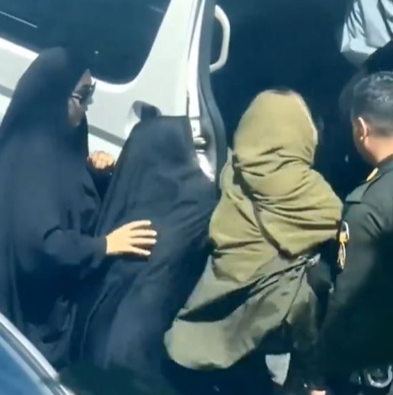 Two women in black shove her into the open vehicle