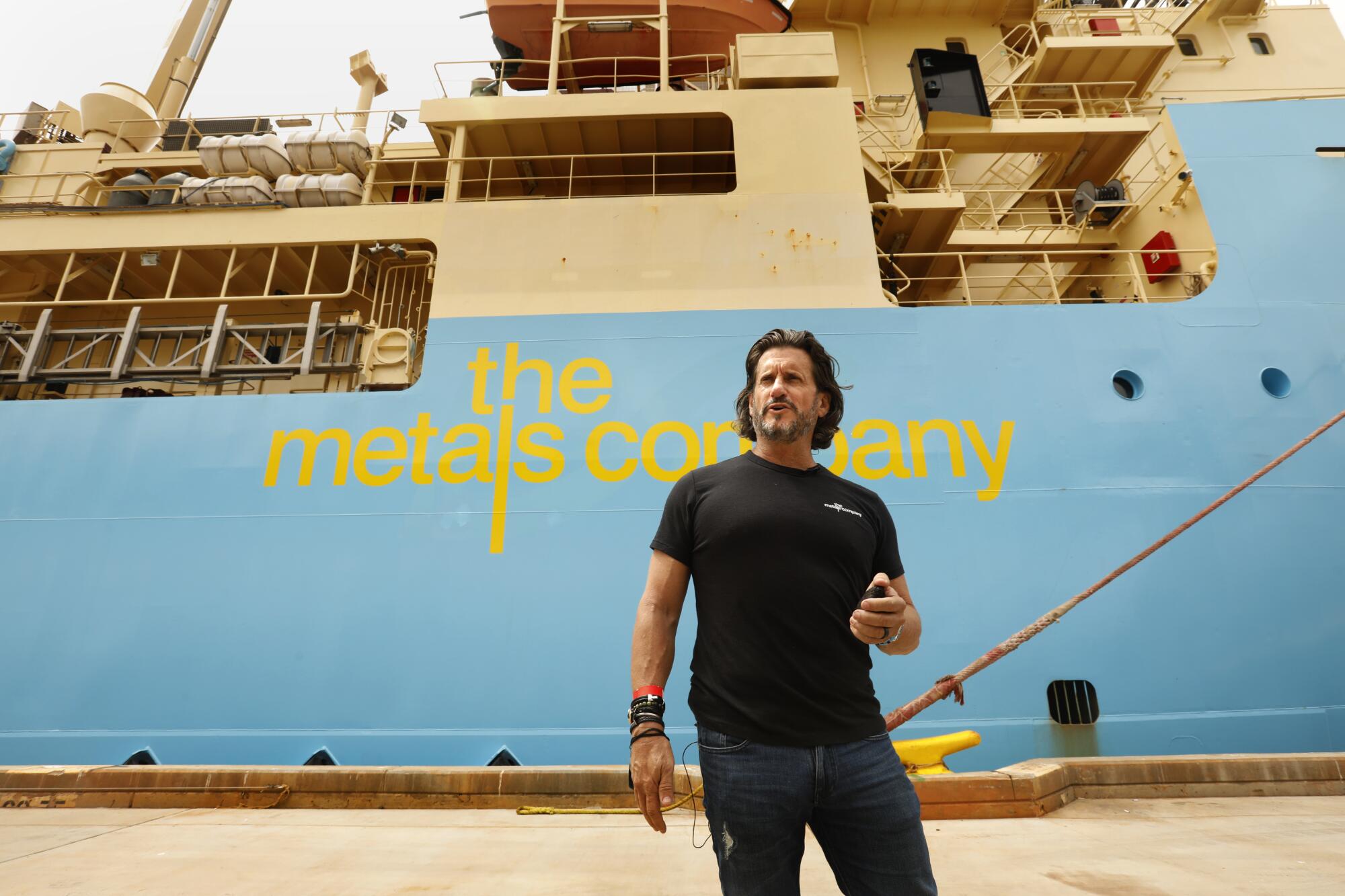 A man stands before a docked ship that bears a logo reading, "the metals company."