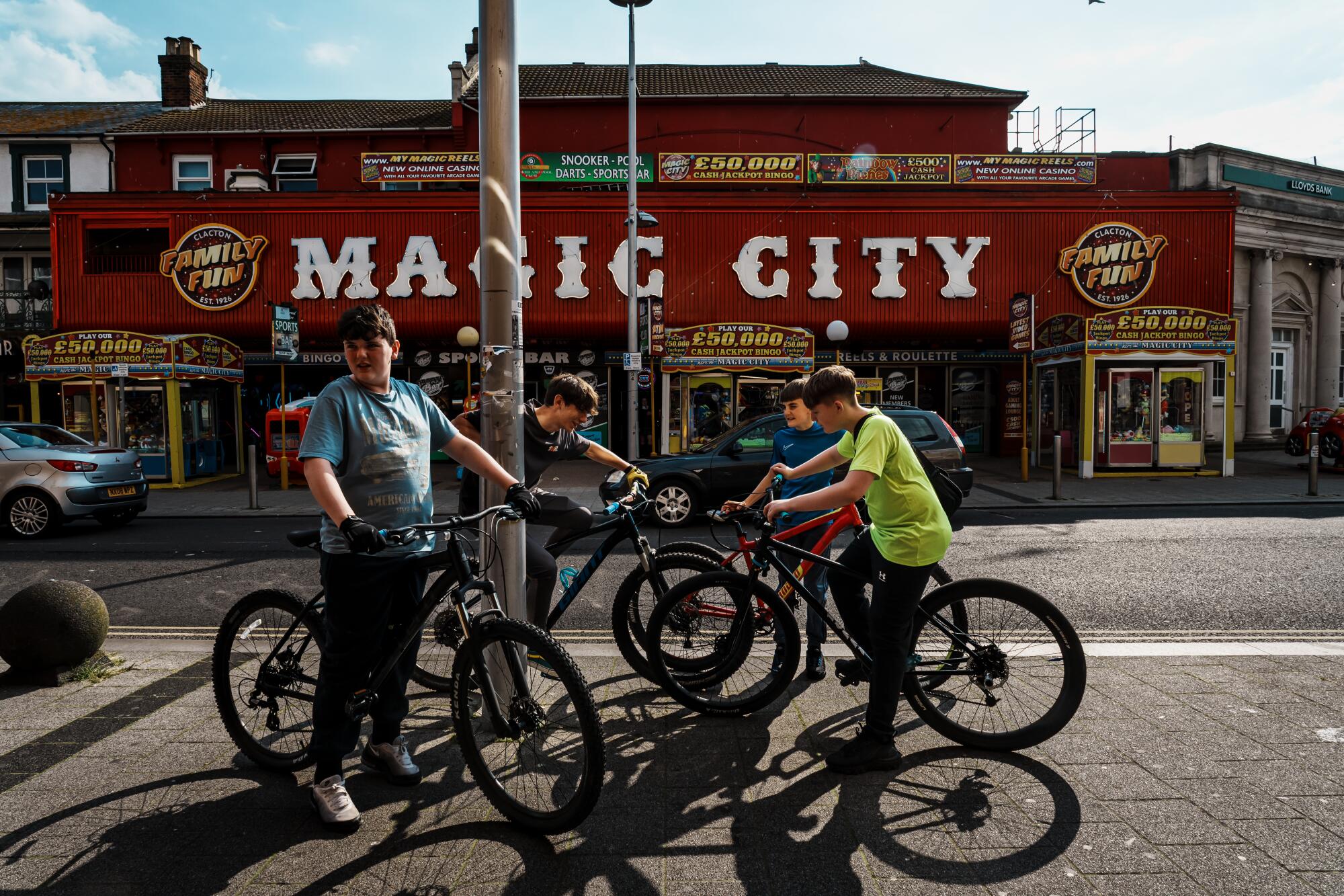 Boys on bicycles hang out on a sidewalk across from a building with the sign Magic City. 