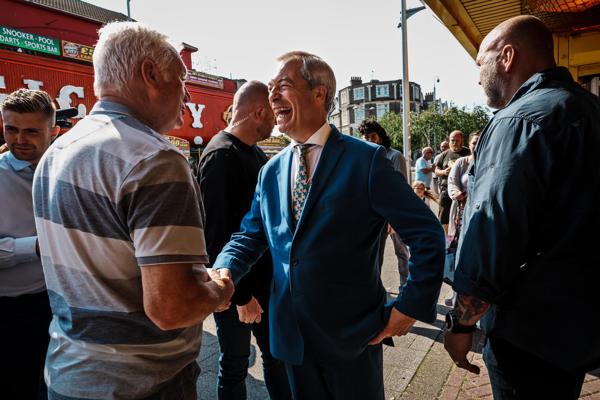 Nigel Farage smiles widely and shakes a man's hand. 