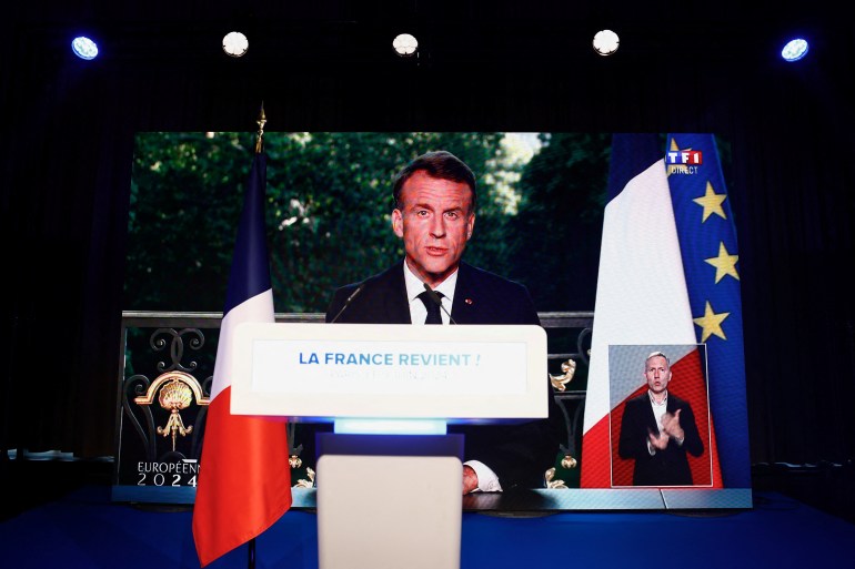 French President Emmanuel Macron speaks through a screen at the far-right National Rally 