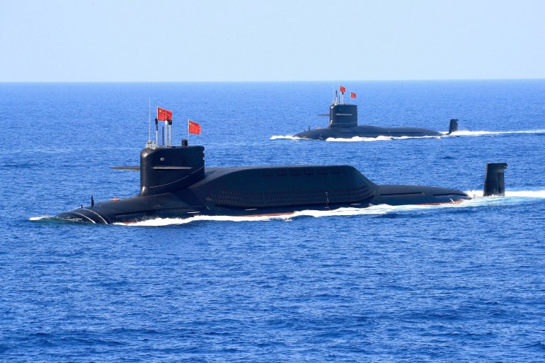 Two nuclear-powered Chinese submarines on the South China Sea. They are on the surface and flying Chinese flags.