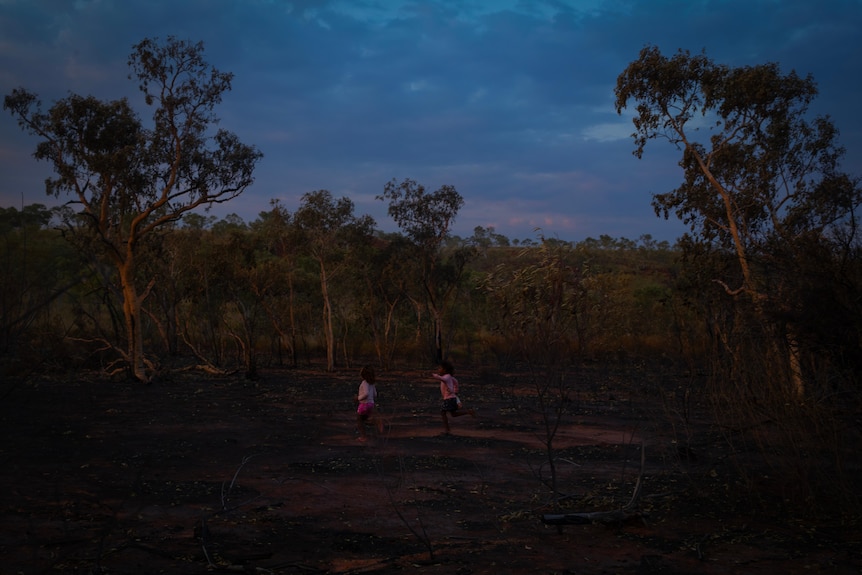 Two girls run in the dark bushland 