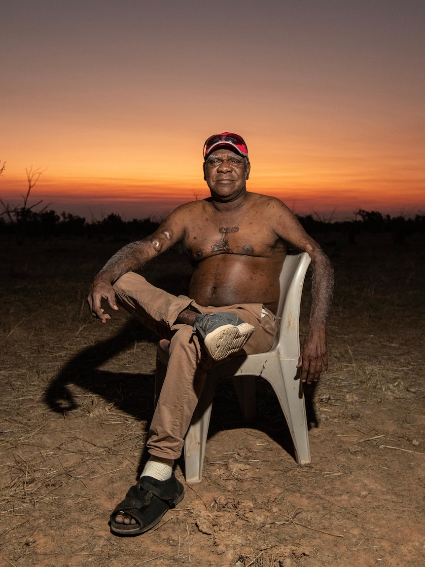 A shirtless man sits in front of the sunset 