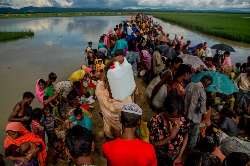 A line of hundreds of Rohingya people carrying belongings and children, stretching into the distance 