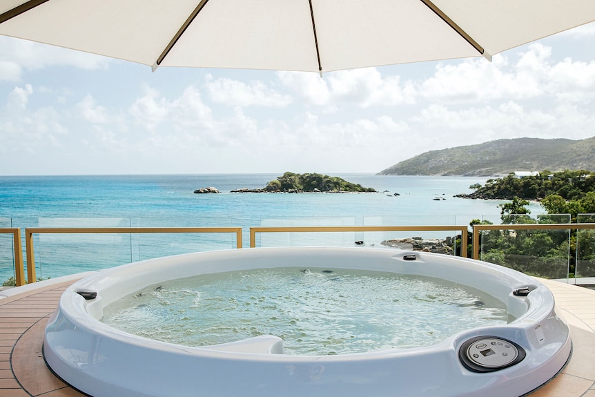 A circular spa overlooking aqua blue seawater with a tiny island in the distance.