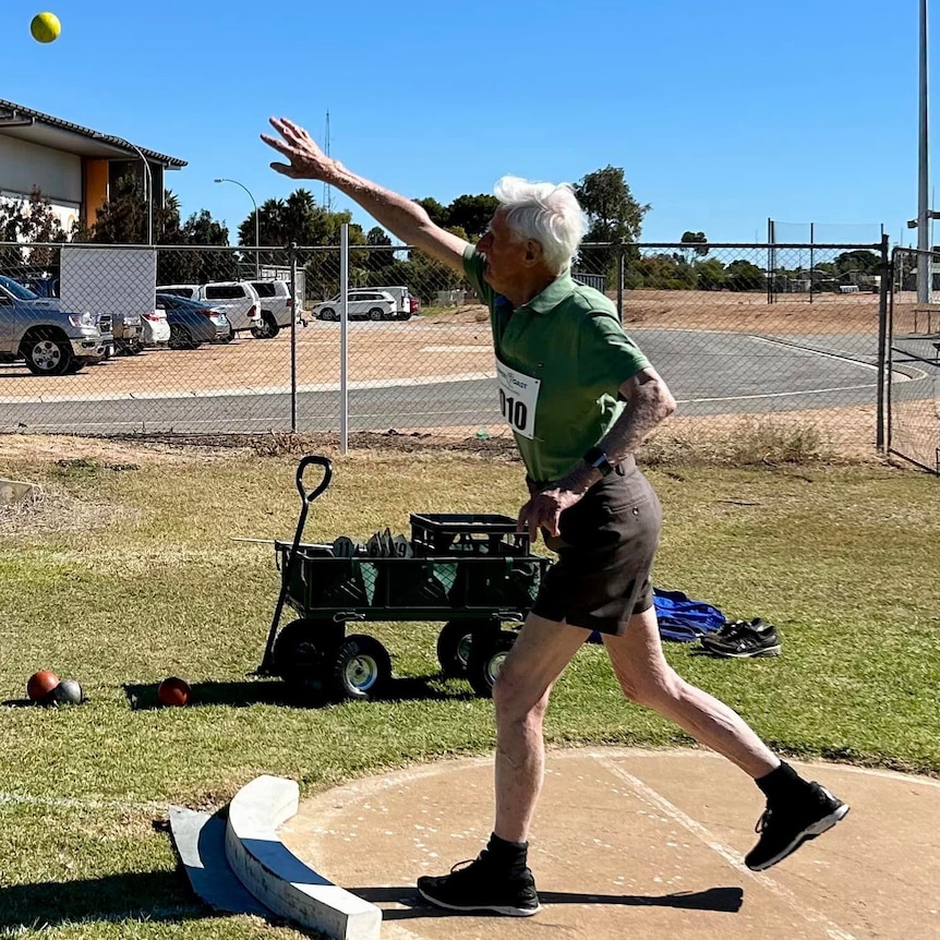an elderly man in a green top and brown shorts throwing a shot put ball 