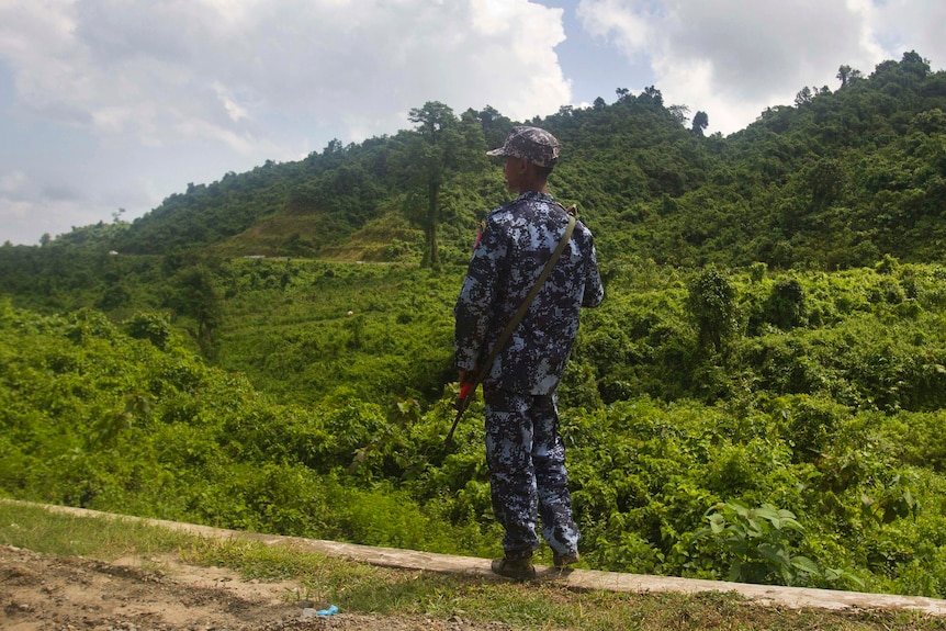 A police officer dressed in a camouflage uniform holds a gun.