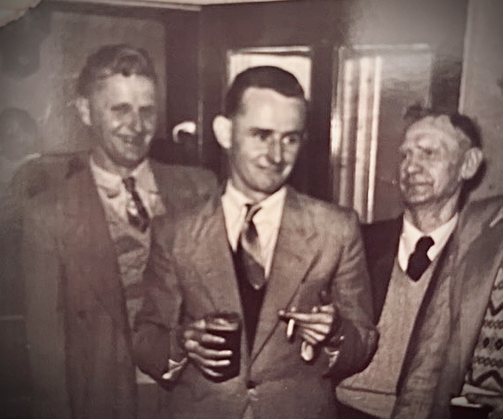 A black and white photo of a man smoking and drinking a beer with two other men watching