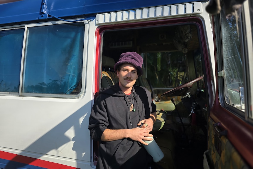 A young man in a hat leans against a seat in a van.