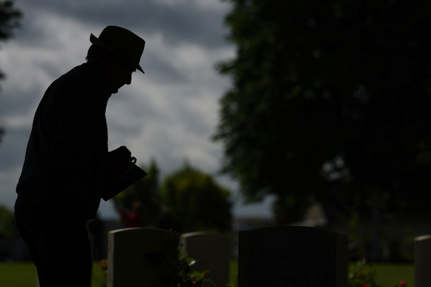 A silhouette of a man stands over a grave 