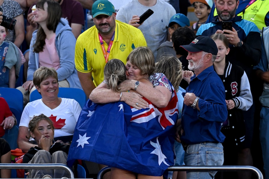 a woman in athletics attire hugs a woman in the crowd at a stadium.