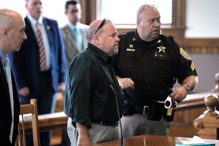 Steve Kramer stands in a courtroom, surrounded by a lawyer and a law enforcement officer.