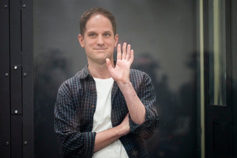 Evan Gershkovich in a glass-walled dock in a Moscow court. He is waving.