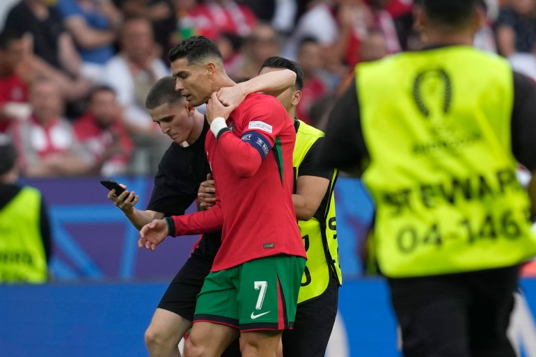 A pitch invader tries to take a selfie with Portugal's Cristiano Ronaldo as a steward moves him out during a Group F match between Turkey and Portugal at the Euro 2024 soccer tournament in Dortmund, Germany, Saturday, June 22, 2024. (AP Photo/Darko Vojinovic)