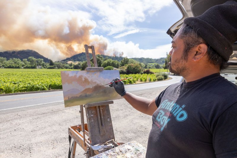 John Paul Marcelo paints a landscape of the Point Fire west of Geyserville, Calif., on Sunday. Fast-moving wildfires, pushed by high winds, hit dry landscapes forcing evacuations as California enters the fire season. Photo by Peter DaSilva/UPI