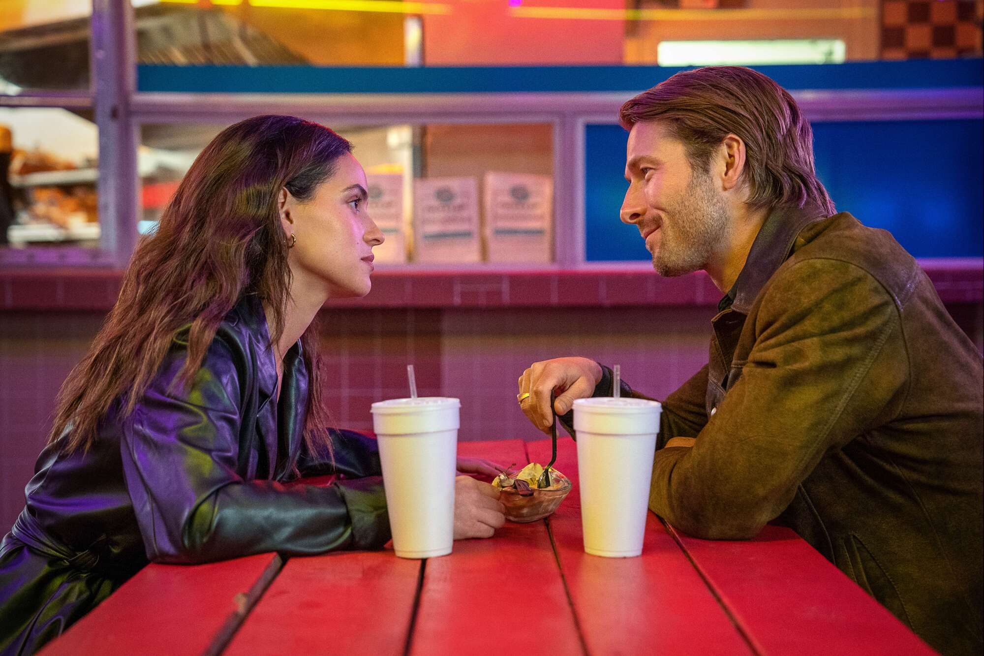 A young woman and young man sit across from each other at a table and gaze into each other's eyes.