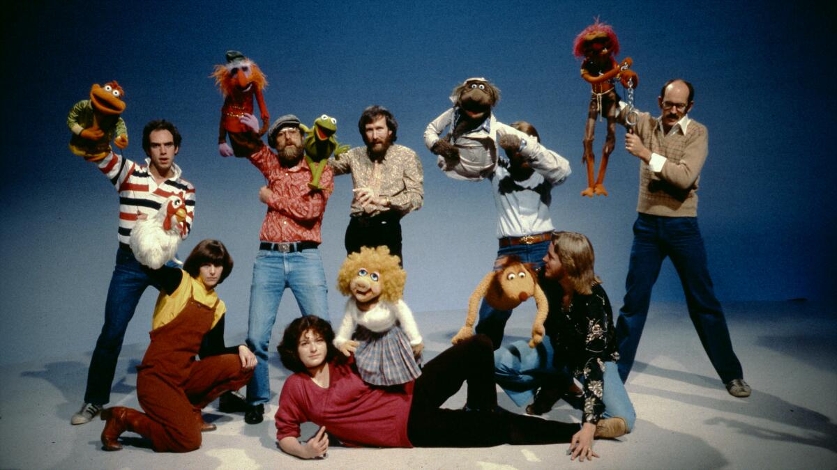 Jim Henson and his team hold up a variety of his Muppet creations